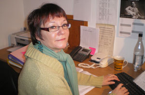 Image of a woman sat at her office desk, facing towards the camera