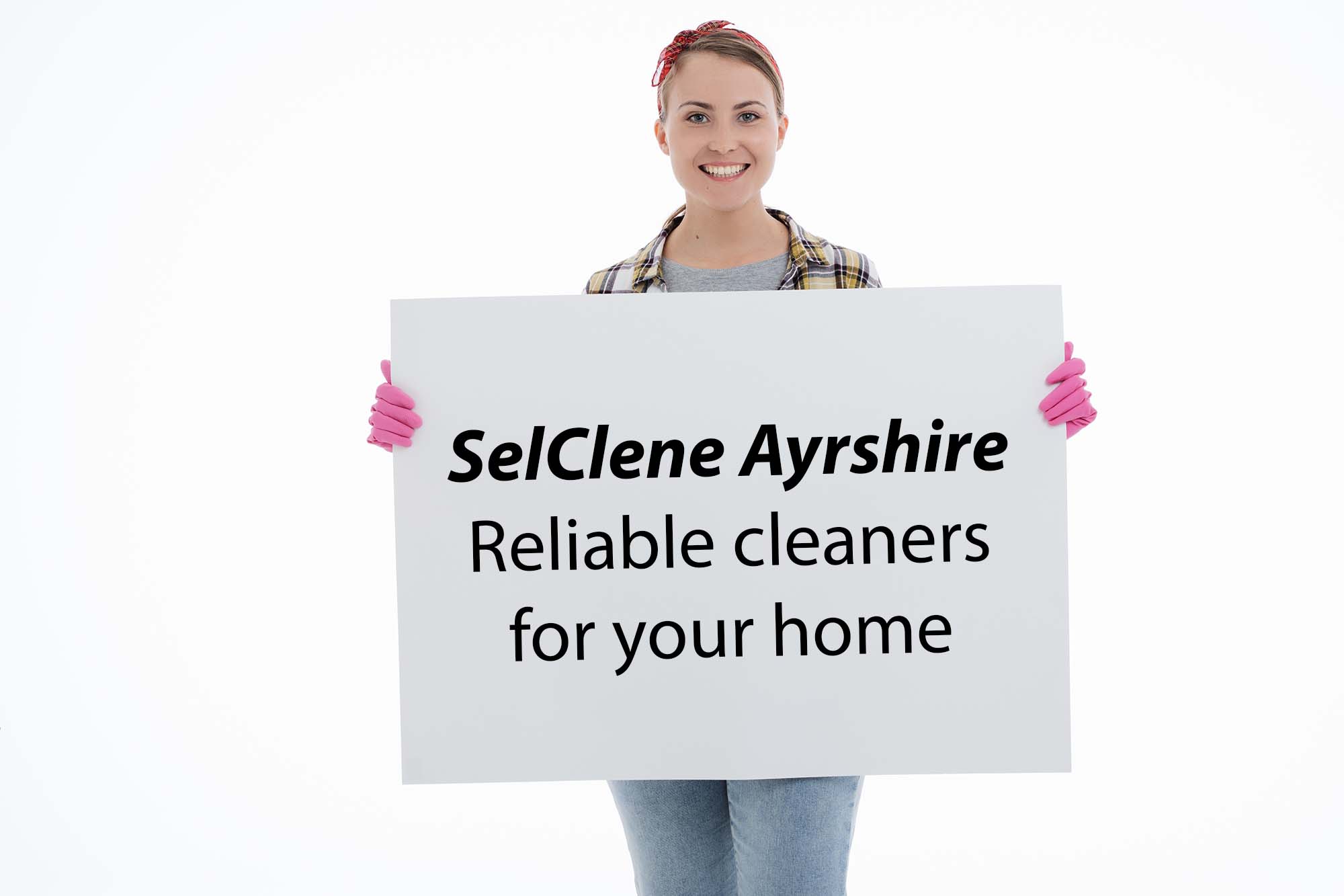 Image of a woman facing the camera dressed as a cleaner and holding us a notice board promoting SelClene Ayrshire
