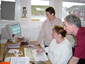 Image of three people standing over at desk and studying a computer screen